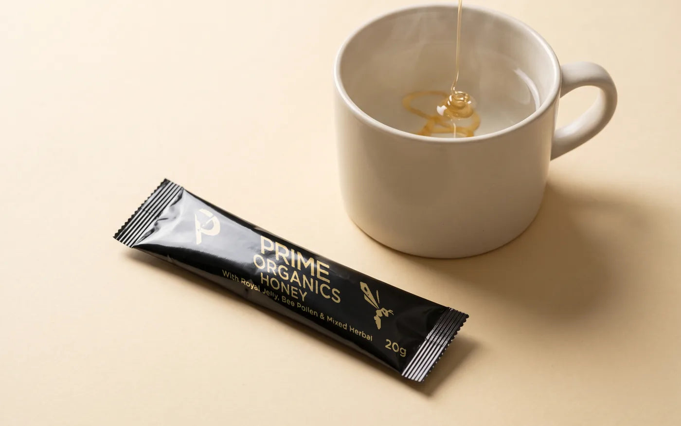 A sealed Prime Organics Honey sachet beside a mug of warm water with honey being stirred in